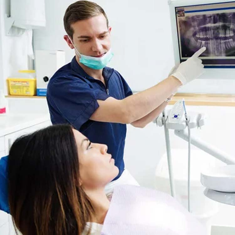 Dentist examining patient's teeth in modern dental office with X-ray images visible.