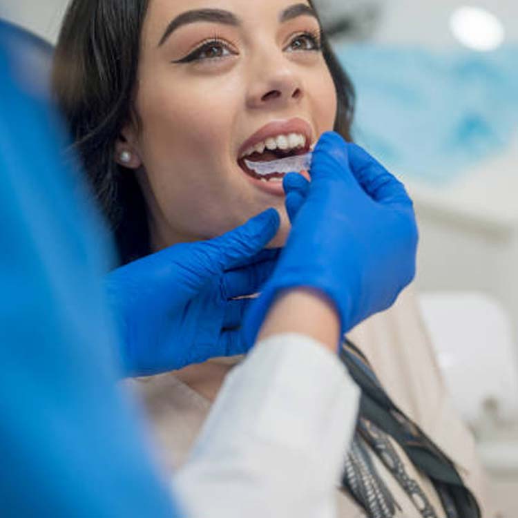 Woman receiving dental examination in bright clinical setting with blue gloves visible.