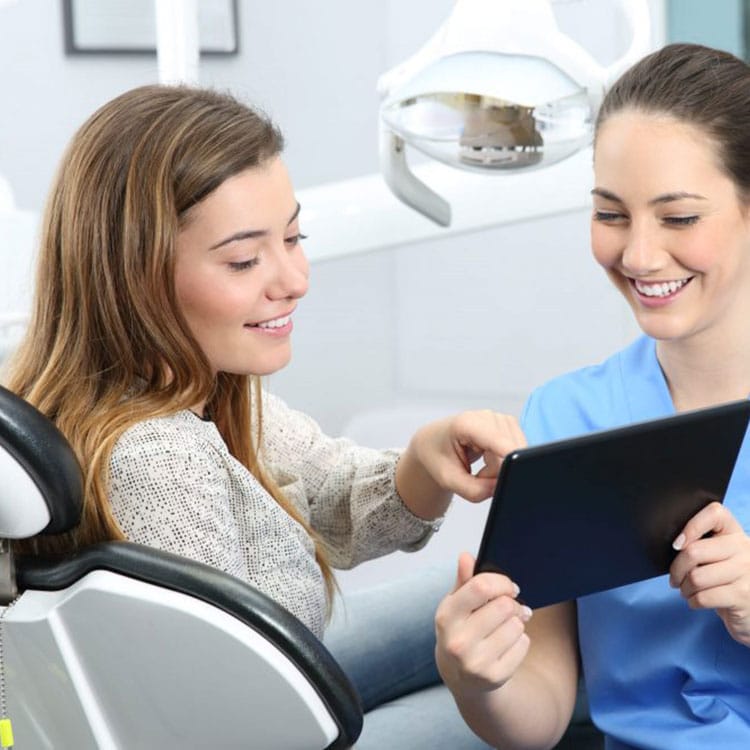 Dental hygienist showing patient treatment plan on tablet in modern dental office.