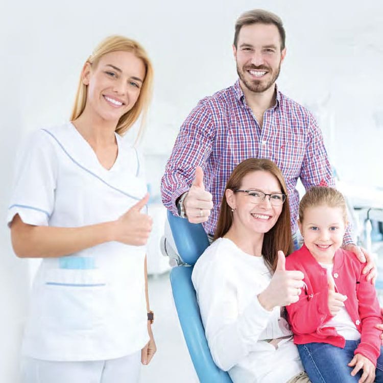Dental professional with family showing thumbs up in modern clinic setting