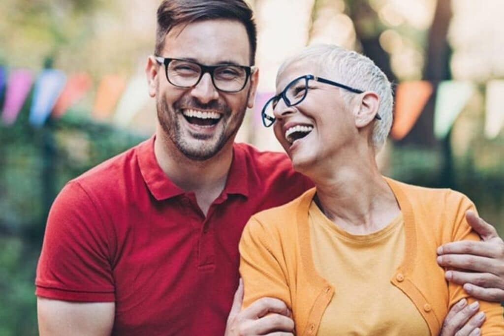 Young man and elderly woman laughing together outdoors in casual clothing.