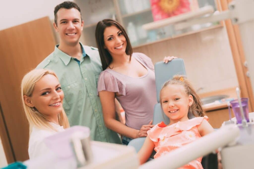 Family smiling at dental office with dentist and staff during checkup visit.